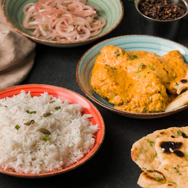 Indian butter chicken, rice, naan, and pickled onions on a dark table at Shangrila Restaurant.