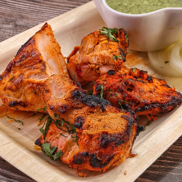 Indian chicken tikka, charred and garnished with cilantro, served with green chutney and sliced onions.