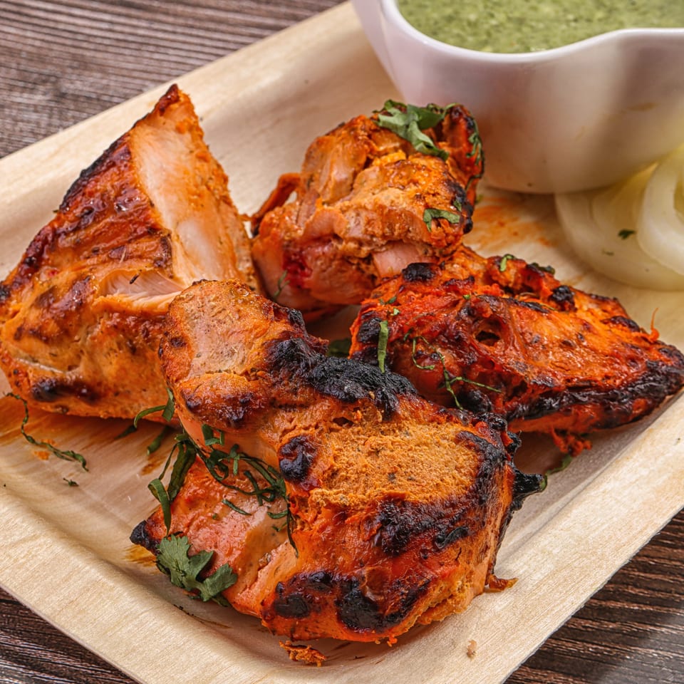 Indian chicken tikka, charred and garnished with cilantro, served with green chutney and sliced onions.
