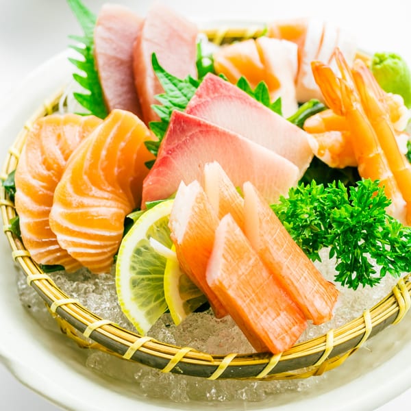 Assorted sashimi platter with salmon, tuna, shrimp, and crab sticks, garnished with lemon and parsley.