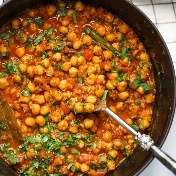 Close-up of Indian chana masala in a black pan, garnished with fresh cilantro and a green chili.