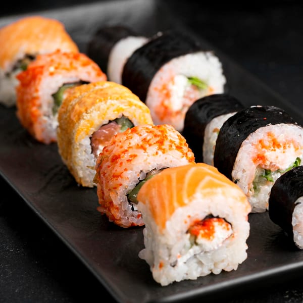 A close-up of various sushi rolls with salmon, roe, and seaweed on a dark plate.