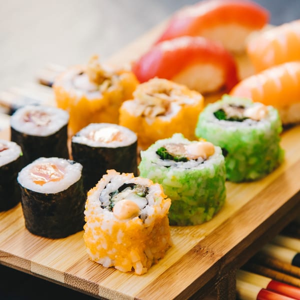 A wooden board displays various sushi rolls, including maki and nigiri, with colorful toppings.