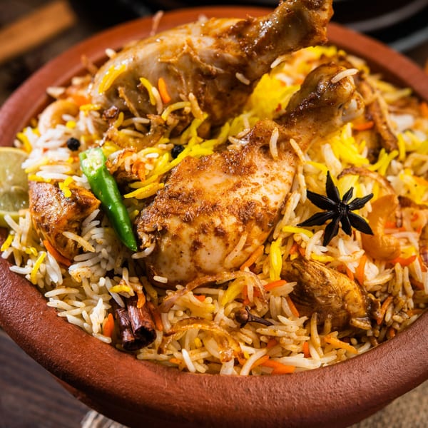 Chicken Biryani in a clay pot, garnished with star anise, green chili, and lemon.
